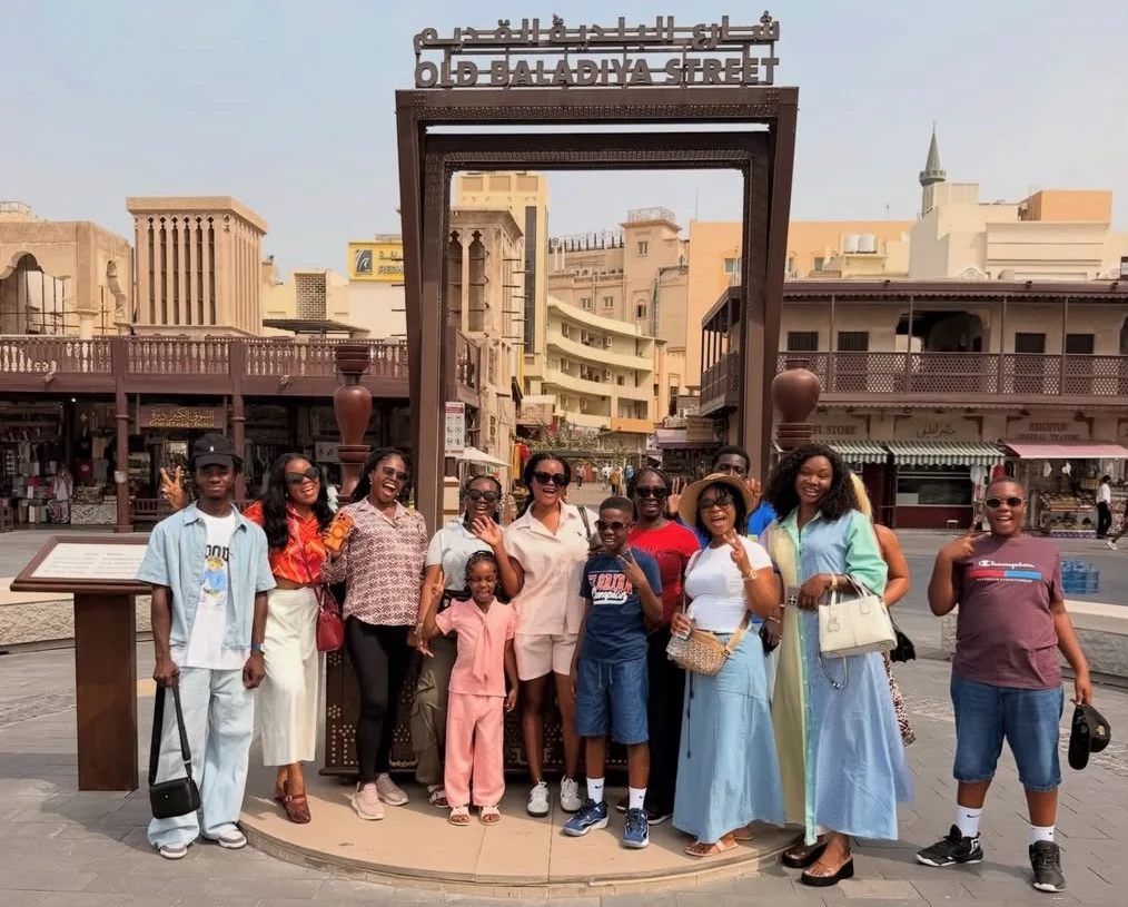 A Myma Travels group of adults and children smiling together under the Old Baladiya Street sign in Dubai