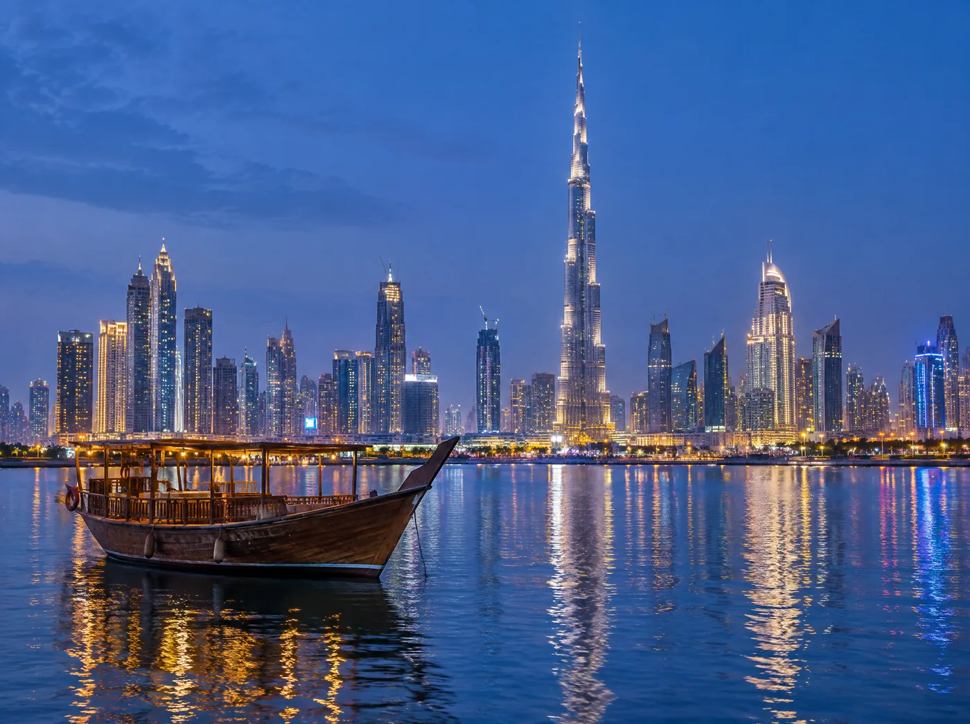 The Dubai skyline lit up at dusk behind a wooden dhow